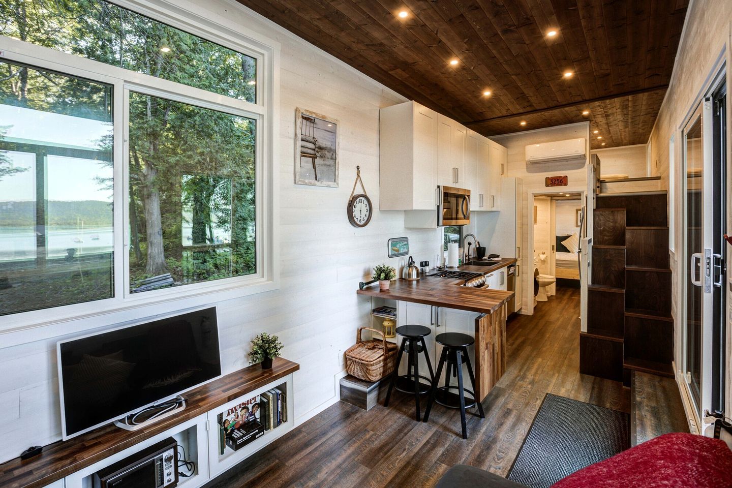 Une cuisine moderne avec un îlot central en bois, des meubles blancs et une grande fenêtre donnant sur une forêt.