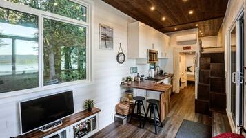 A modern kitchen with a wooden island, white cabinetry, and a large window overlooking a forest.