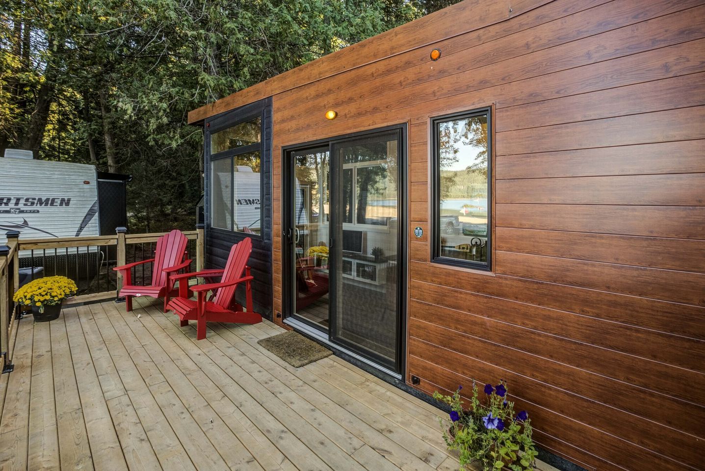 A wooden deck with two red chairs and a potted plant.