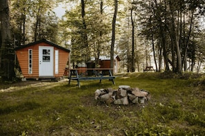 A rustic cabin with a wooden exterior, a small porch, and a picnic table in a forested area.