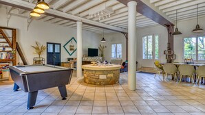 Amplio espacio interior con mesa de billar, barra de piedra y zona de comedor con sillas y mesa.