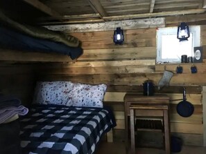 Una habitación de cabaña de madera con una cama, una mesita pequeña, un farol colgante y una ventana.