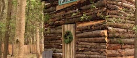 A rustic log cabin with a porch, a fire pit, and a chair.