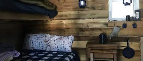 Una camera in legno con un letto, un tavolino, una lanterna appesa e una finestra.