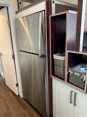 Un refrigerador de acero inoxidable, una cesta de mimbre y un gabinete blanco con tiradores plateados.