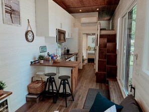 Una cocina compacta con microondas, una isla de madera con taburetes y un reloj colgado.