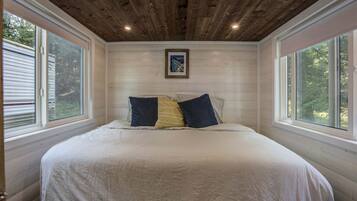 A bedroom with a large bed, two windows, a wooden ceiling, and a framed picture on the wall.