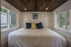 A bedroom with a large bed, two windows, a wooden ceiling, and a framed picture on the wall.
