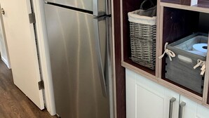 Un refrigerador de acero inoxidable con congelador incorporado, una cesta de mimbre y un gabinete blanco con dos cajones.