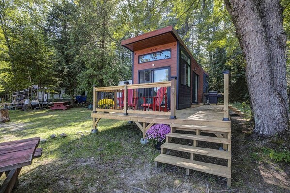 A modern cabin with a deck, surrounded by trees.