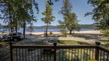 A deck with a view of a lake, trees, and a parked car.