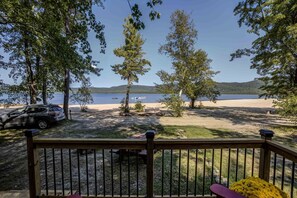 A deck with a view of a lake, trees, and a parked car.