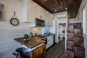 A compact kitchen with white cabinets, a stainless steel microwave, and a wooden island with stools.