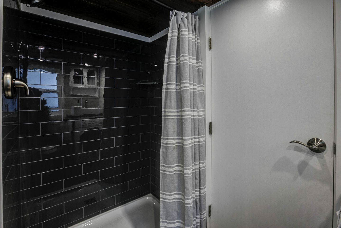 A bathroom with black tiled walls, a white door, and a shower curtain.