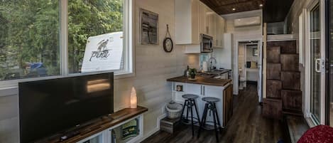 Una cocina moderna con una isla central, taburetes de bar y un televisor en un estante empotrado.