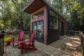 Una terraza moderna de madera con puerta de vidrio, sillas Adirondack rojas y una parrilla.