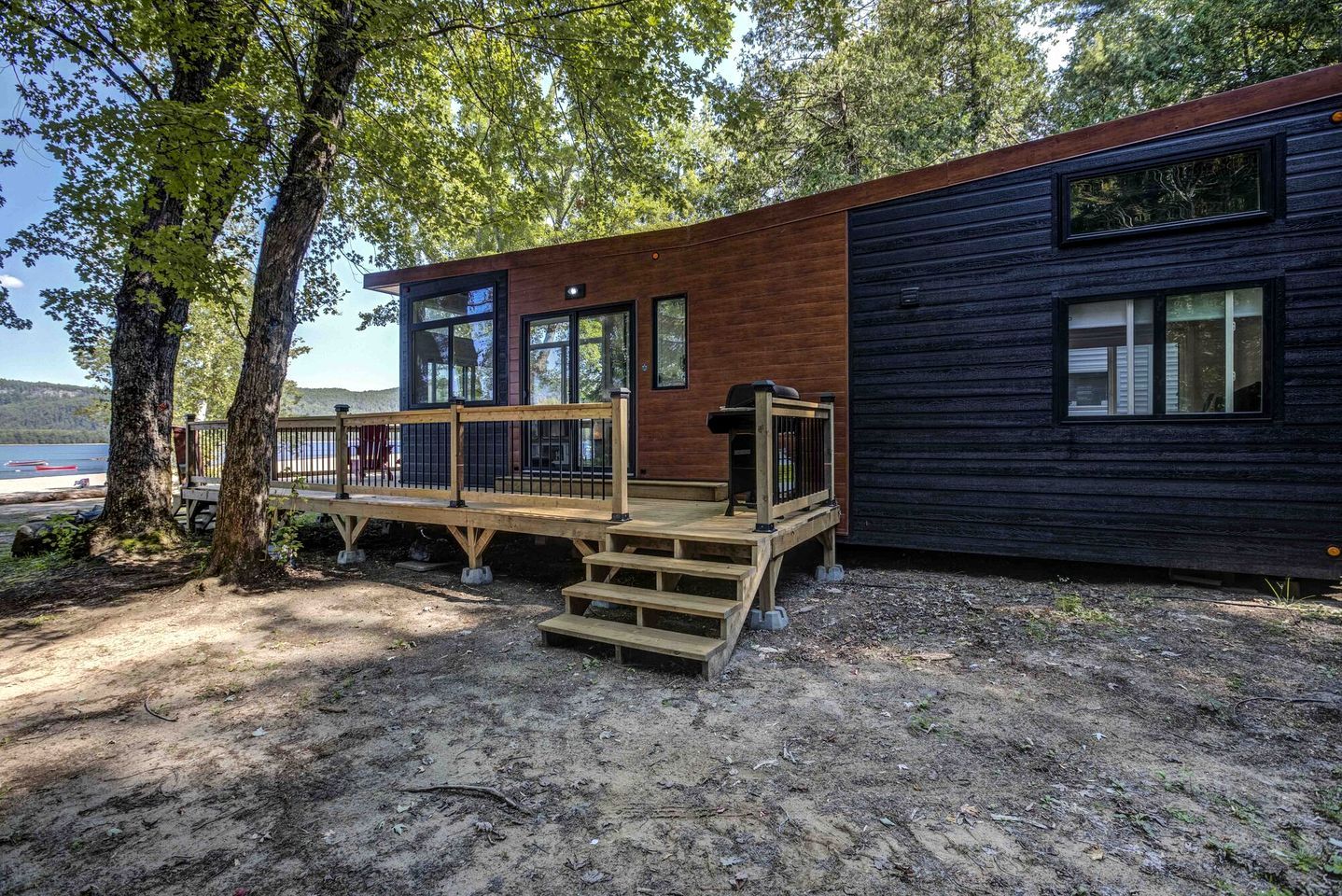 A cabin with a wooden deck, large windows, and a view of the water.