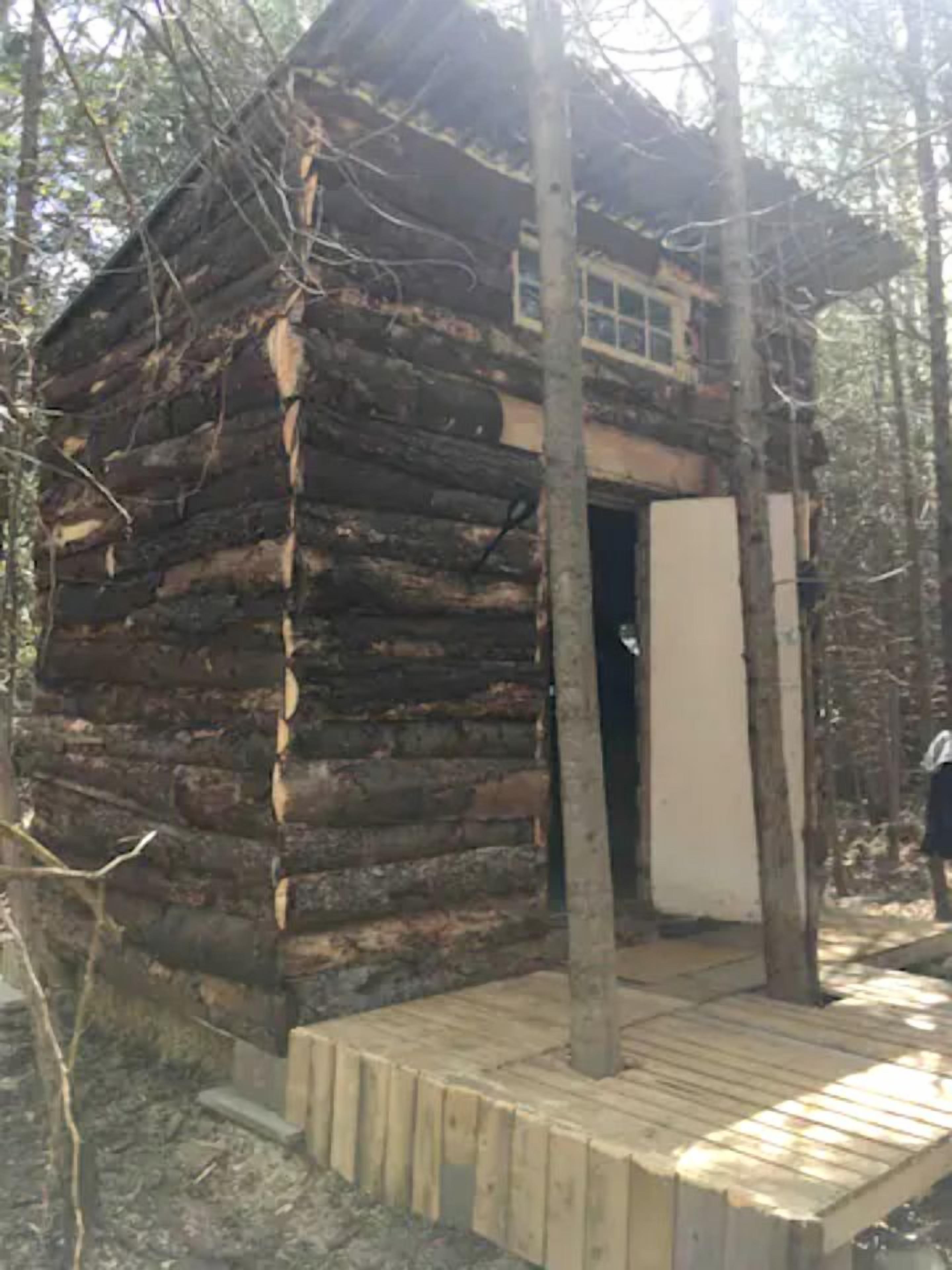 A rustic log cabin with a wooden deck and a door leading to the interior.
