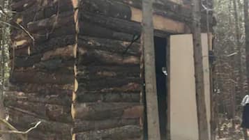 A rustic log cabin with a wooden deck and a door leading to the interior.