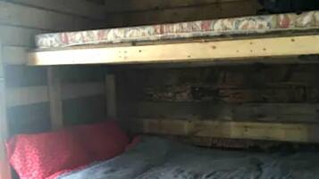 A bunk bed with a red pillow and a blanket, a wooden table, and a black bag hanging on the wall.