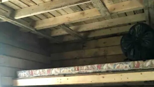 Ein Stockbett mit einem roten Kopfkissen und einer Decke, ein Holztisch und eine schwarze Tasche, die an der Wand hängt.