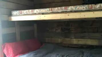 A bunk bed with a red pillow and a blanket, a wooden table, and a black bag hanging on the wall.