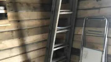 Un coin de pièce aux murs en bois, avec une échelle en métal et une étagère métallique.