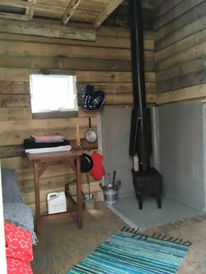A rustic wooden cabin interior with a wooden table, a stove, and a window.