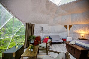 A cozy interior with a bed, seating area, and a view of greenery through a large window.