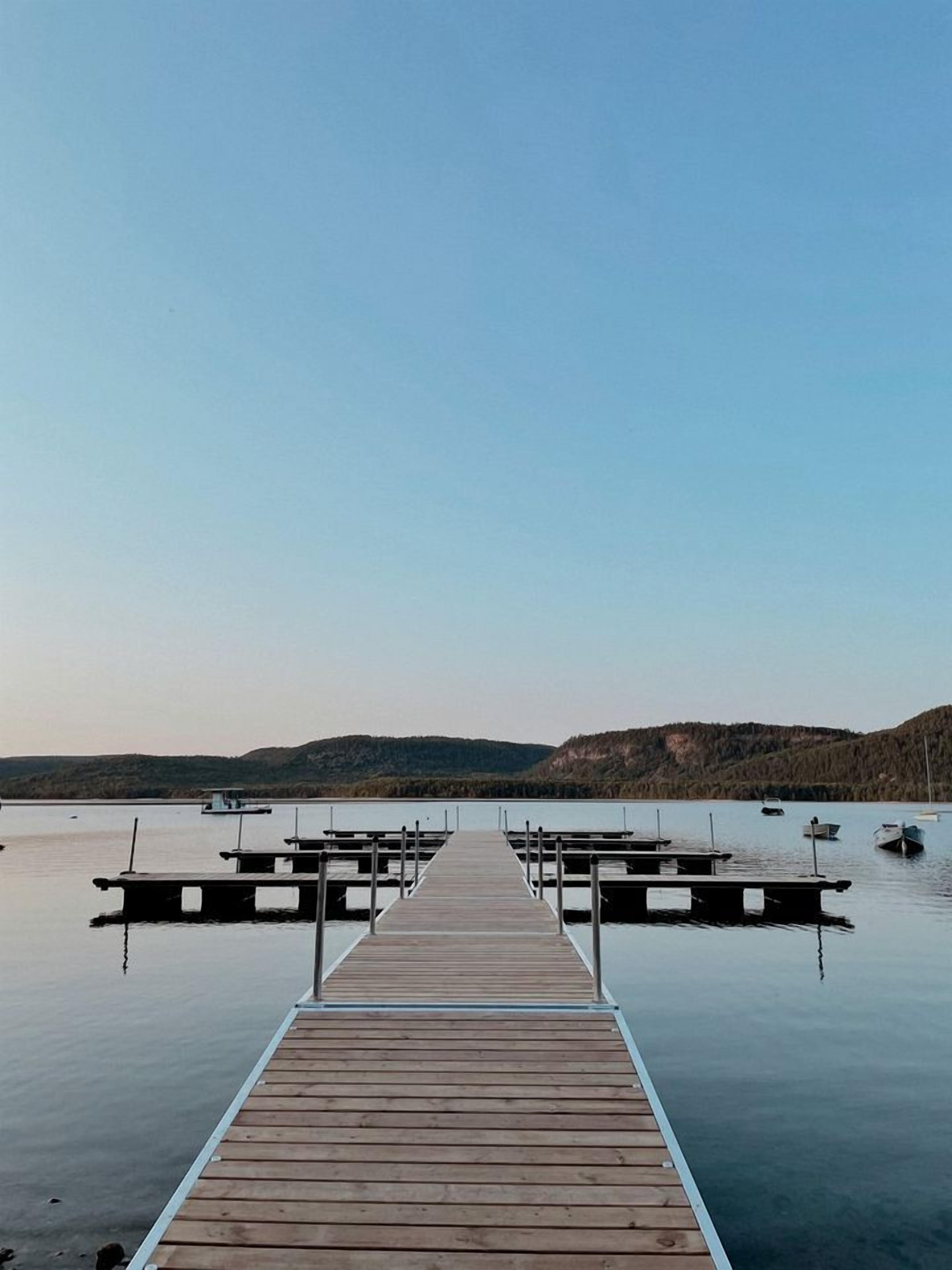 Eine Holzstege, der sich in ruhiges Wasser erstreckt, mit Booten am Ende vertäut.