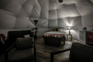 Ein gemütlicher Raum mit geometrischem Muster, ausgestattet mit einem Bett, Nachttisch, Lampe und einer Sitzecke.