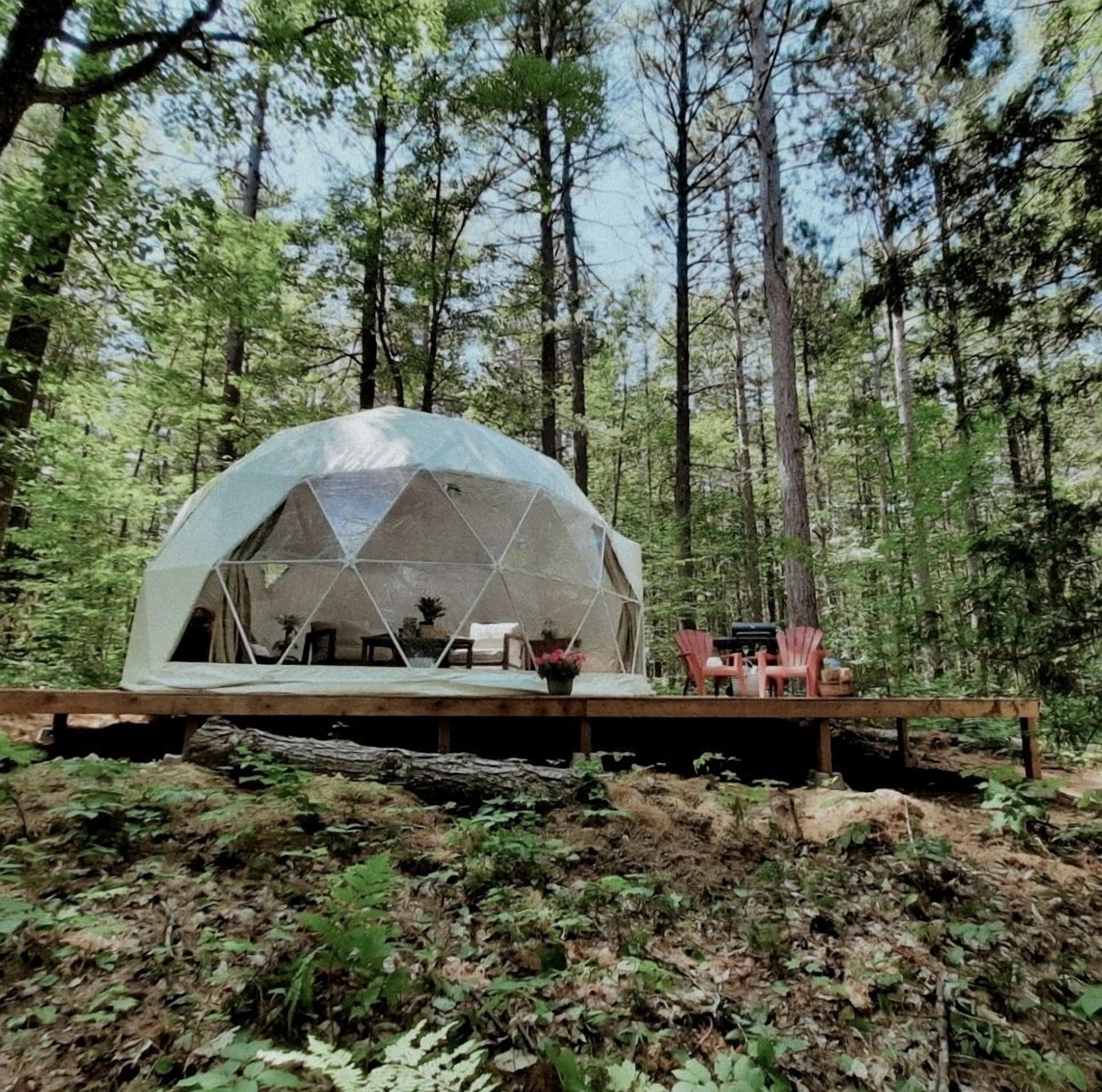 A geodesic dome structure in a forest setting with a deck and outdoor seating.