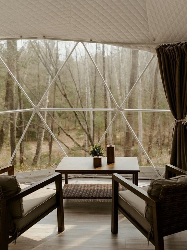 A tent with a table and chairs, a small plant, and a view of a forest. - Fantastic Dome Nestled Amidst Trees and Barbecue Provided in Petawawa, Ontario (Petawawa)