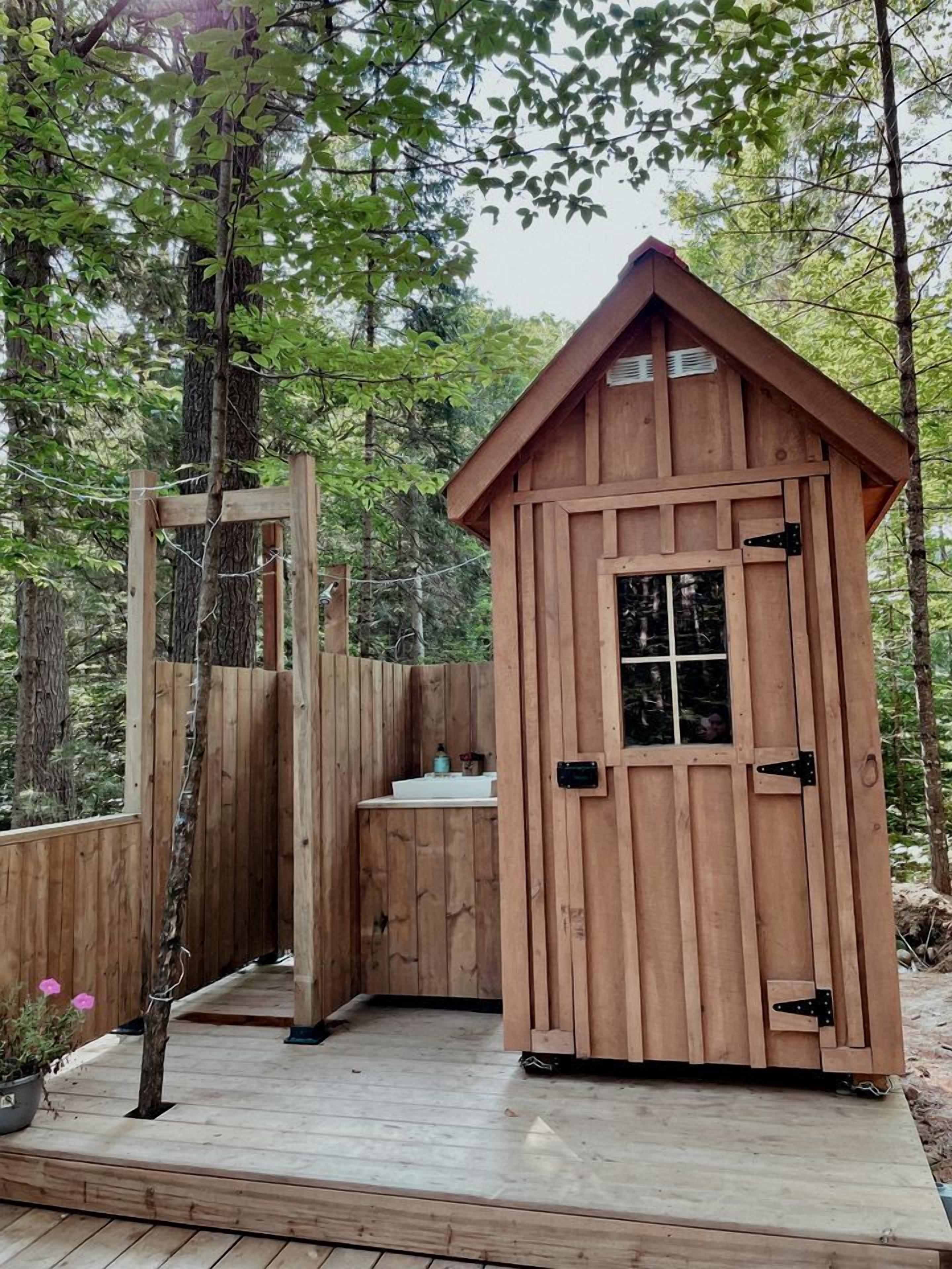 A wooden cabin with a small bathroom, a door, and a window.