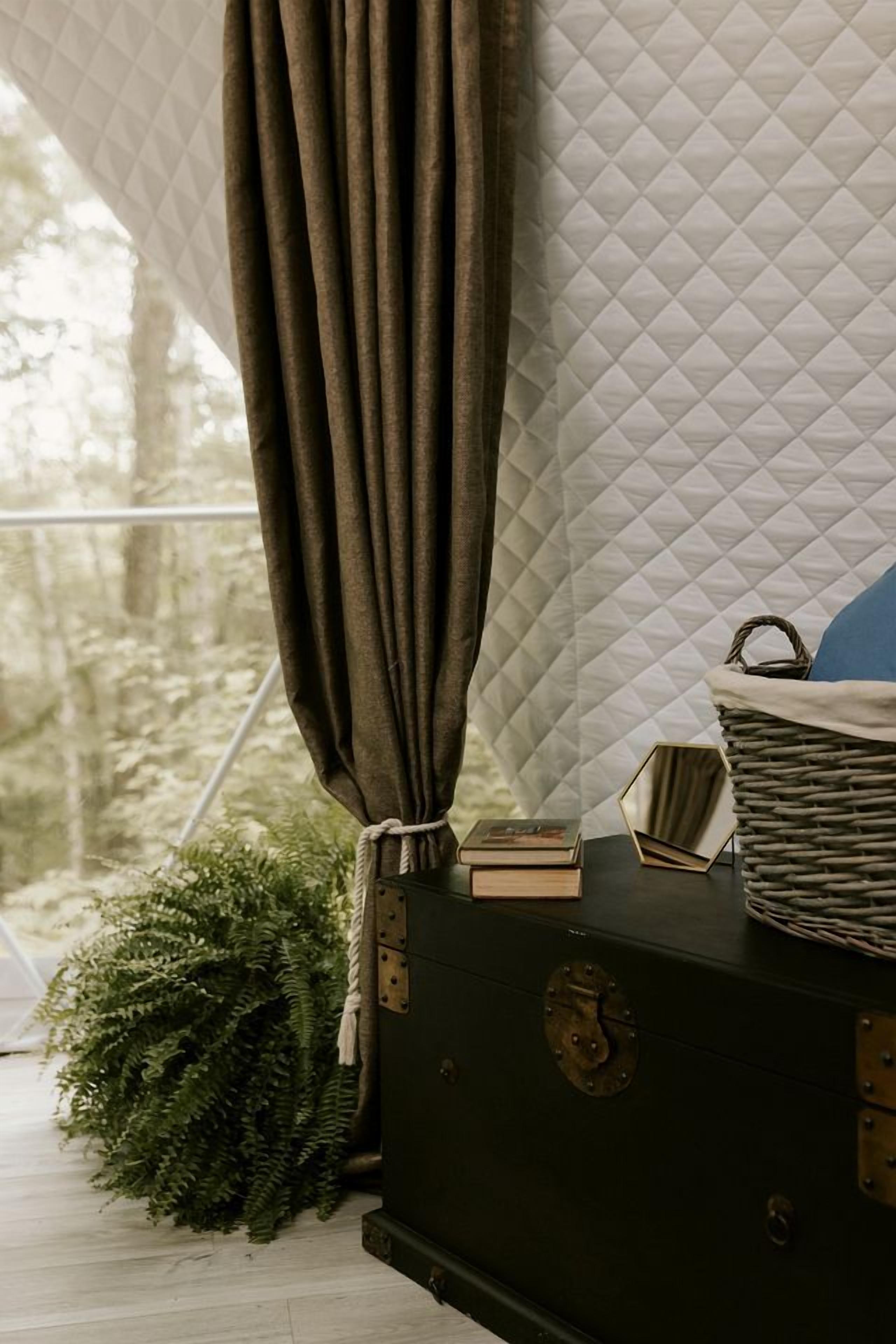 A room with a quilted wall, a dark-colored chest of drawers, a woven basket, and a curtain.