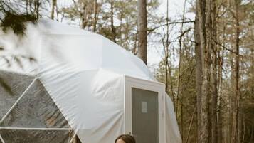 A person meditating on a wooden platform with a tent in a forest.