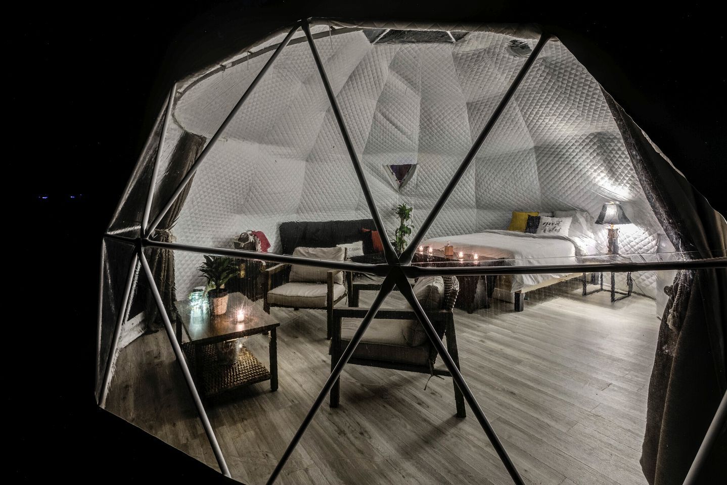 A geodesic dome room with a bed, seating area, and a small table with a plant.