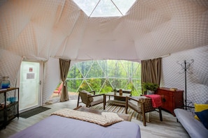Alojamiento en tienda de campaña con cama, zona de estar y vistas al bosque.