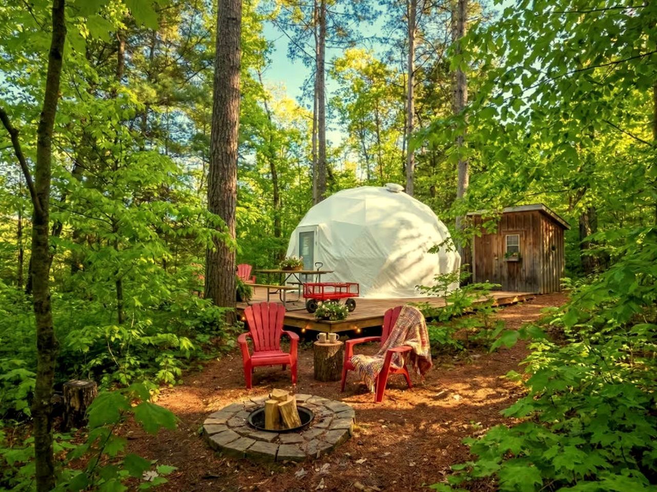 A campsite with a covered tent, a fire pit, and red chairs.