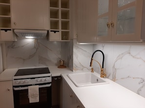 Una cocina con estufa, fregadero, salpicadero de mármol y armarios de colores claros.