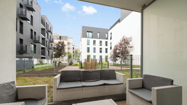 An outdoor seating area with wicker furniture and a view of modern buildings. - Riverfront by Grand Apartments (Gdańsk)