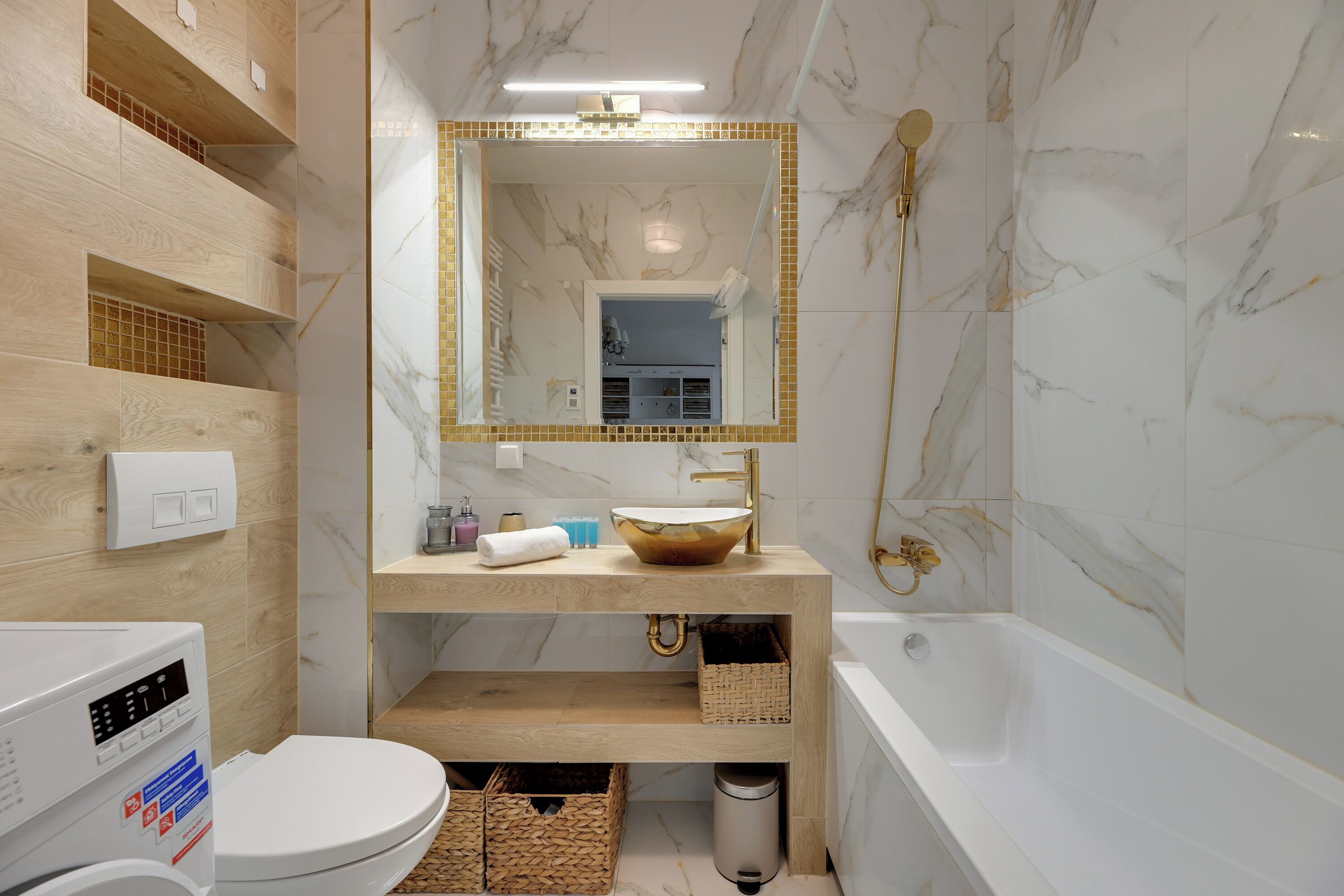 Une salle de bain avec un mur en marbre, un meuble-lavabo en bois, des toilettes blanches et une baignoire.