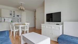 A modern living room with a TV, white furniture, a dining area, and a kitchen. - Riverfront by Grand Apartments (Gdańsk)