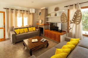 A living room with a sofa, coffee table, TV, fireplace, and decorative leaves. - Can Damià _ San Josep _ Ibiza (Sant Josep de sa Talaia)