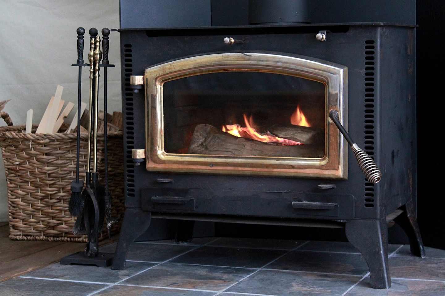 Un poêle à bois noir, doté d’une porte en verre, d’une poignée en métal et d’un feu à l’intérieur.