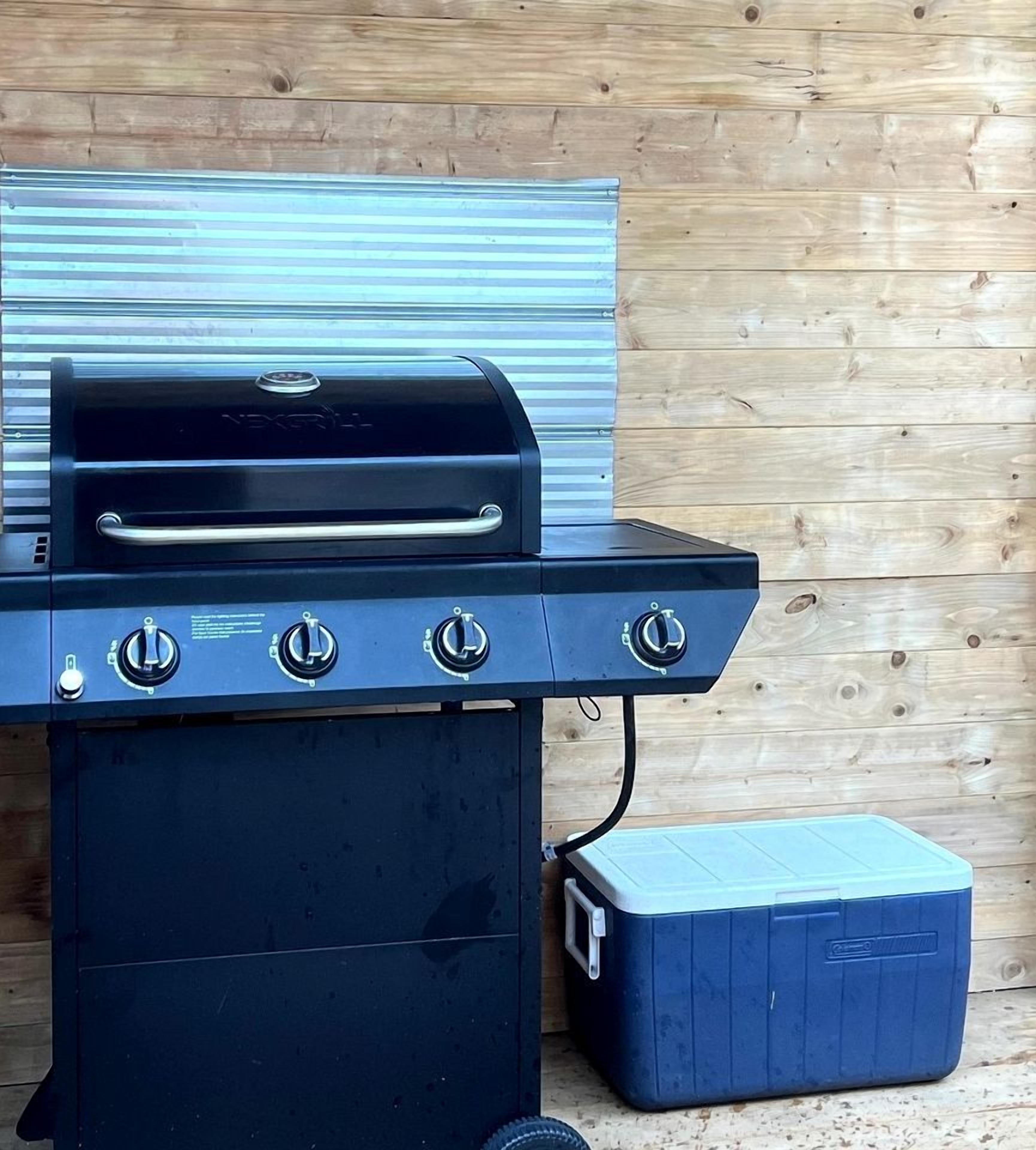 A black grill with three knobs and a side compartment, set against a wooden wall.