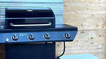 A black grill with three knobs and a side compartment, set against a wooden wall.