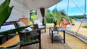 A geodesic dome structure with a wooden deck, wicker furniture, and a view of a river.