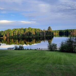A tranquil lake with a grassy foreground and dense forest in the background.