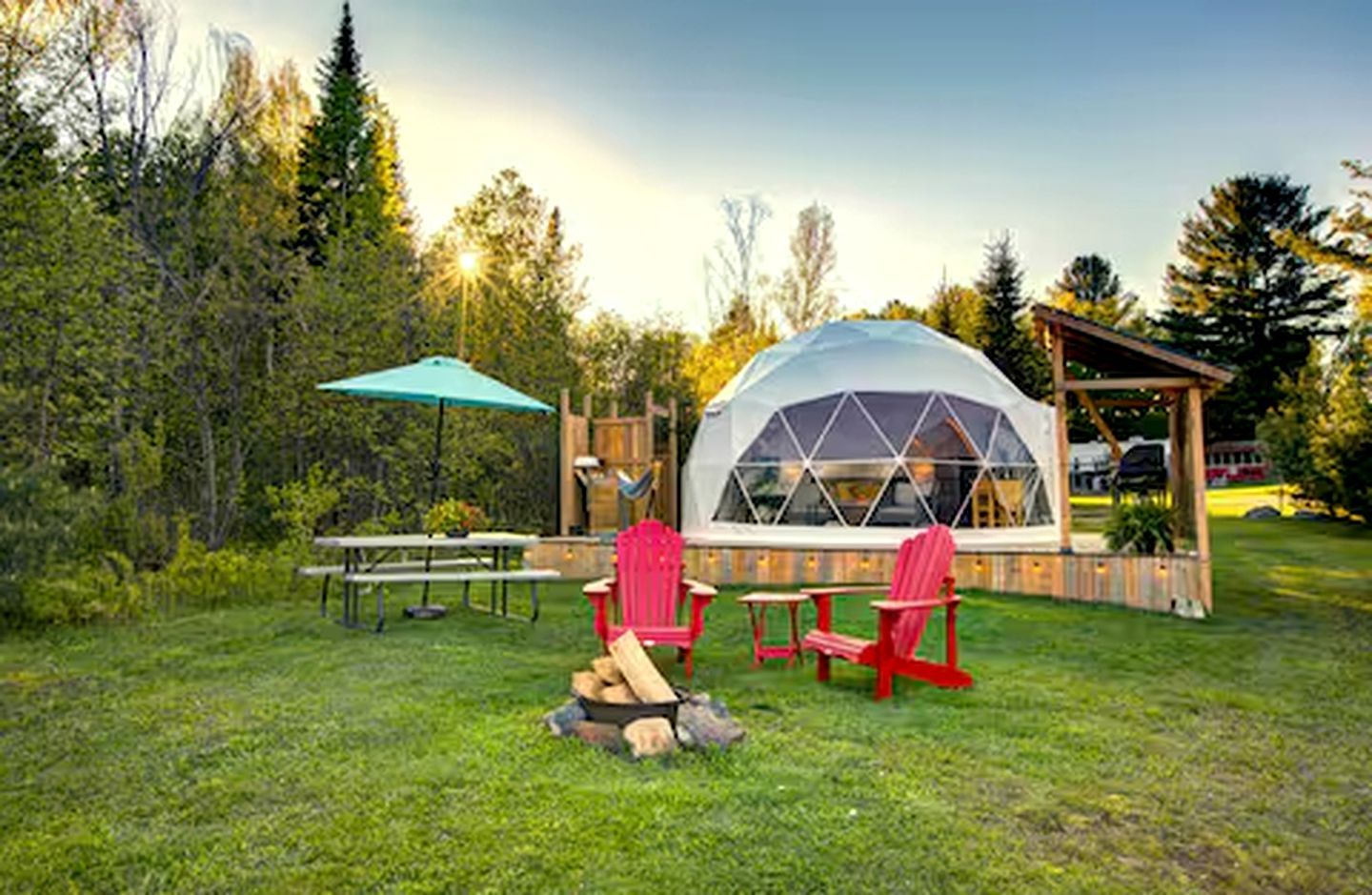 A dome-shaped structure with a transparent roof, surrounded by a grassy area with picnic tables and red chairs.
